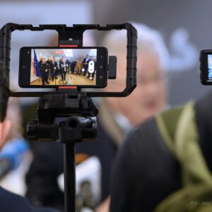 Uczestnicy konferencji prasowej na granicy w Barwinku na ekranie telefonu komórkowego.